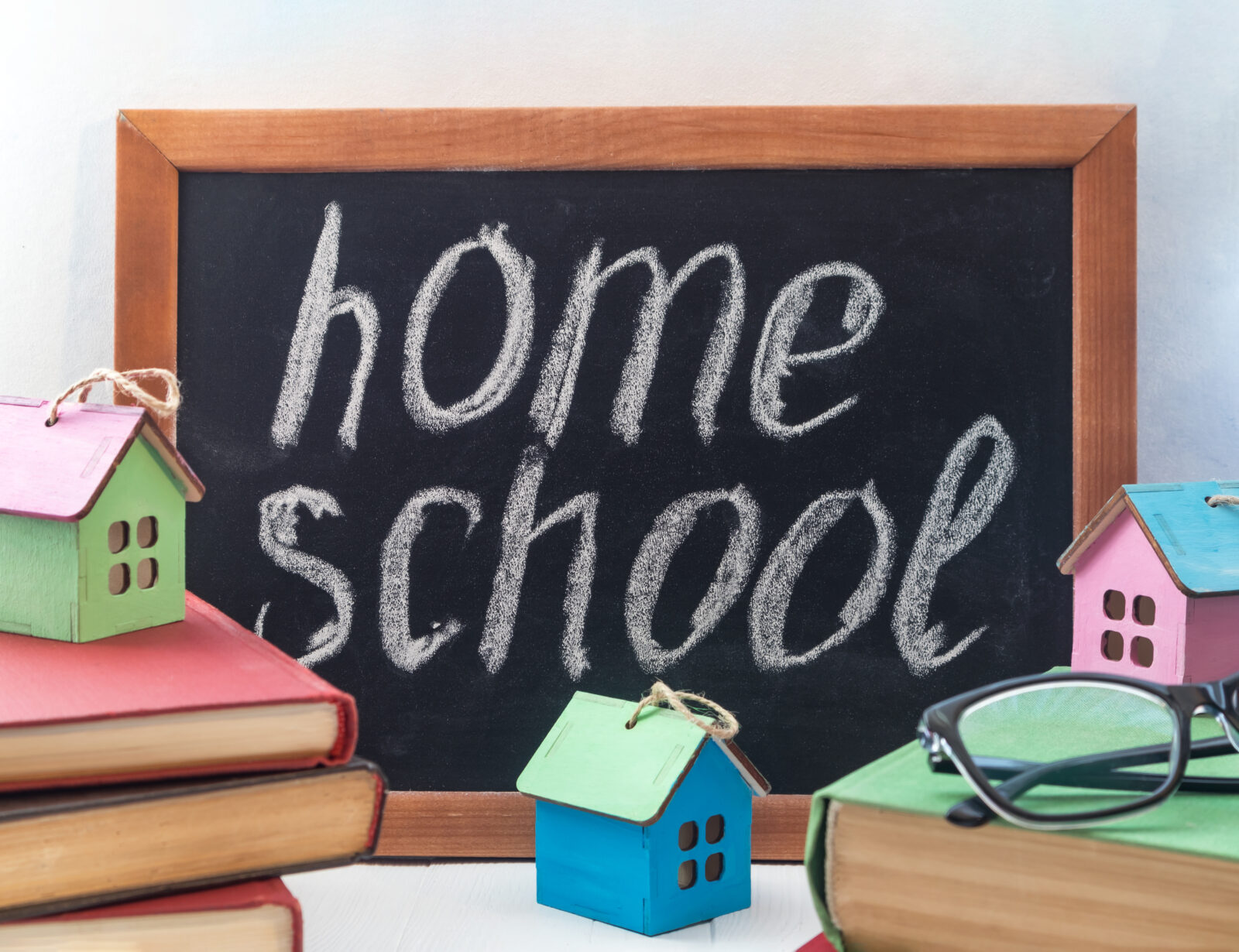 Tabletop chalk board with the word "homeschool" written in white chalk, surrounded by books and colorful wooden house models.