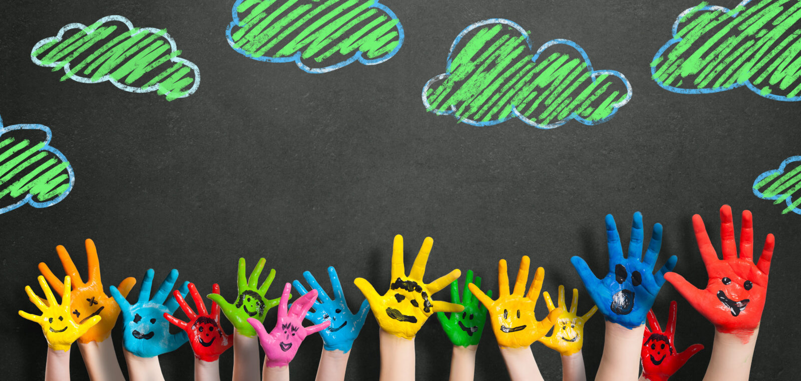 Children's hands painted all different colors with faces painted on in black. Against a black board with green clouds drawn above the children's hands.