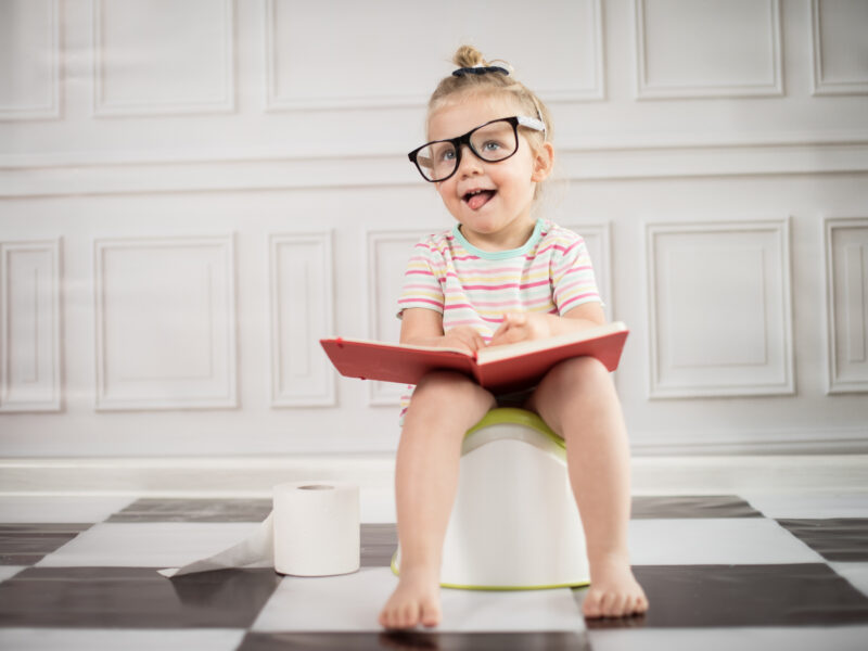 little girl on the toilet wearing glasses and holding a book