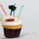 Cupcake with four colorful candles, a graduation cap, and the word congrats on it