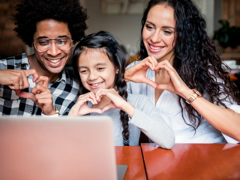 Parents and child forming heart shapes with hands while video chatting