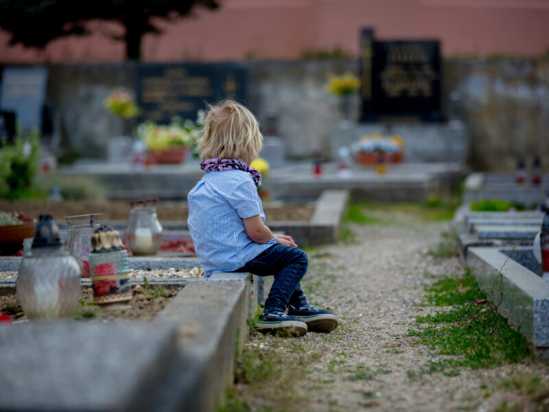 Little boy sitting on grave looking in to the distance