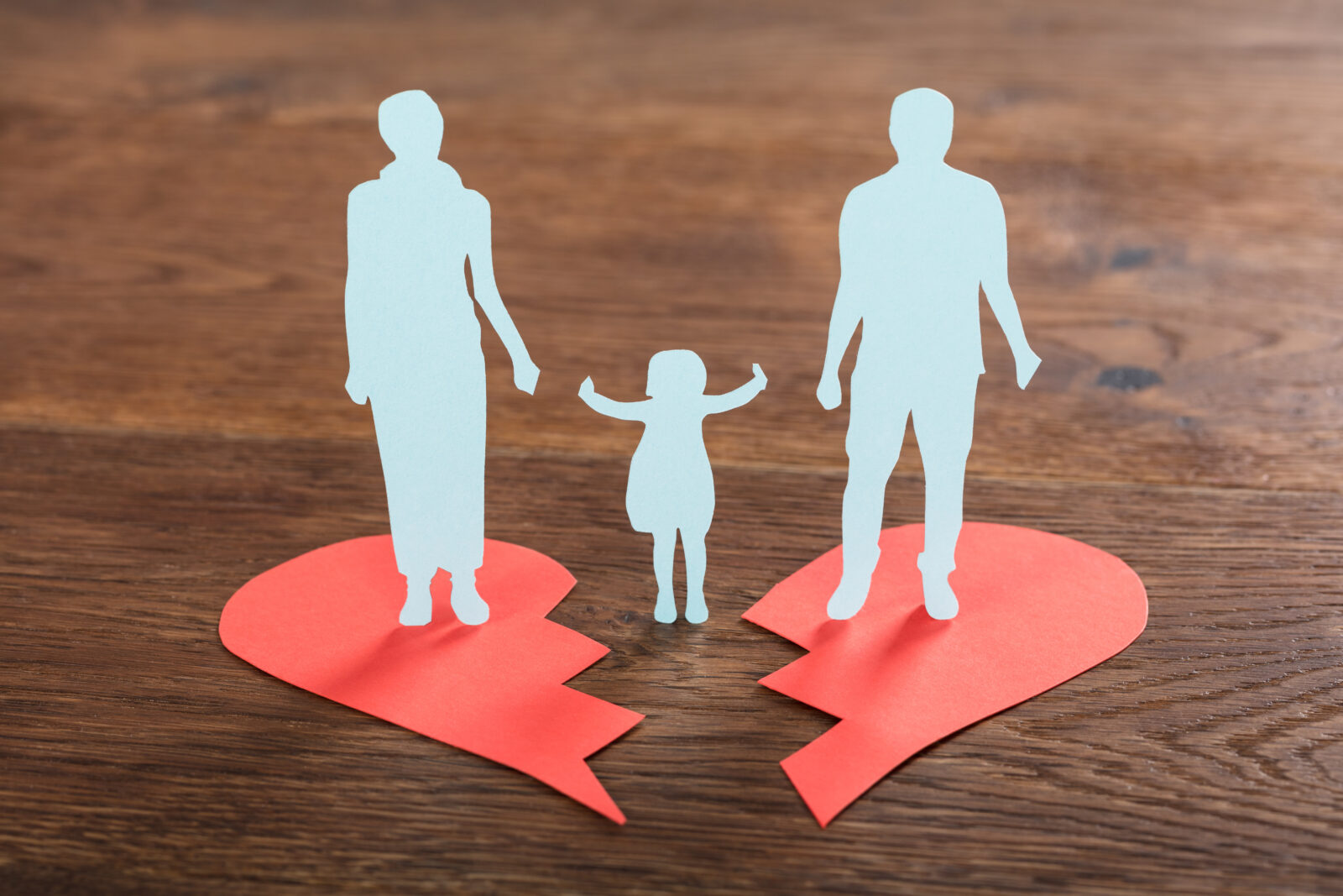 paper heart, broken in half, with a parent standing on each half and a child in the middle reaching out for a hand