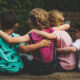 back view of a group of preschool friends sitting in a line with arms around each other