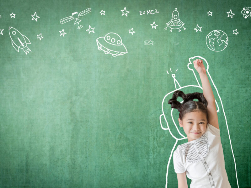 child standing in front of chalkboard, with an astronaut suite drawn around her, souring up towards drawing of spaceships and stars