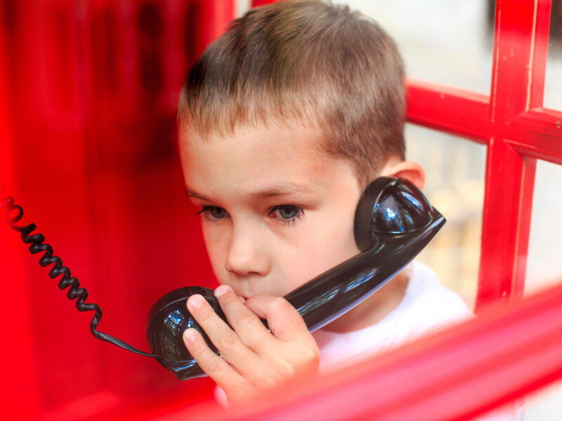 Child using a corded phone in a phone booth