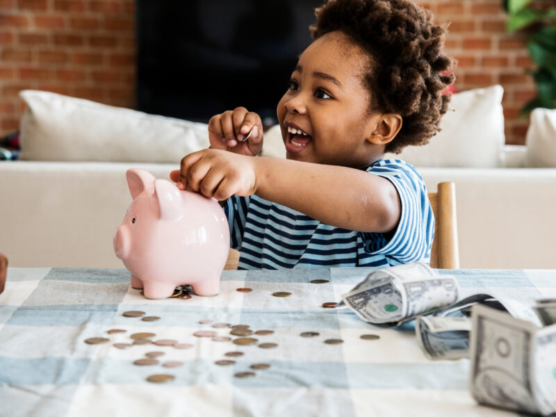 Excited little boy putting coins in a piggy bank
