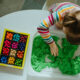 Little girl sorting colored beads from a sensory tray full of green sand