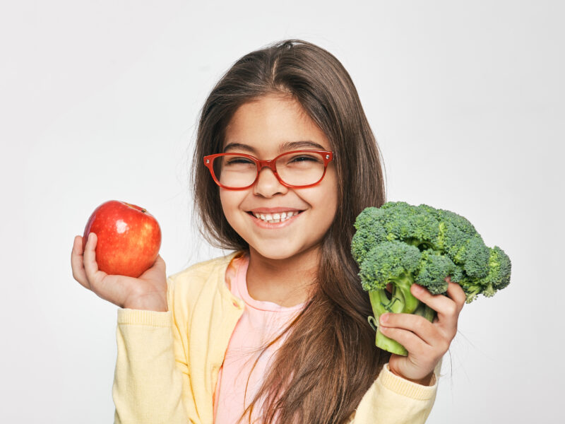 Little girl holding an apple and broccoli