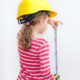 little girl in a hard hat using a tape measure