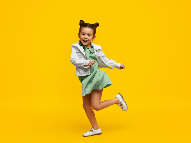 Little girl dancing against a bright yellow background