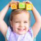 Little girl holding ABC blocks over her head and smiling