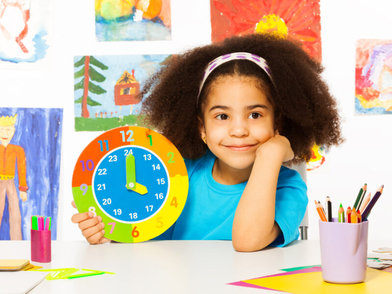 Little girl sitting at a desk holding a colorful clock