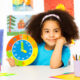 Little girl sitting at a desk holding a colorful clock
