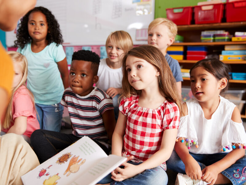 Children sitting on the floor listening to their teacher read them a book