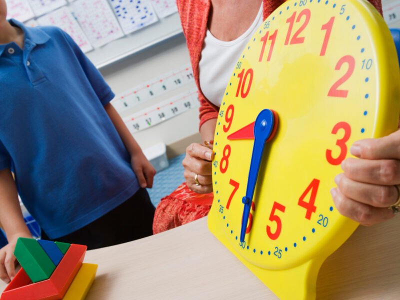 Teacher showing a child how to tell time on a big yellow clock